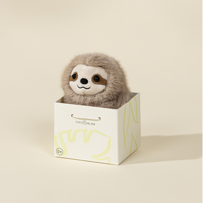 Plush sloth toy in a decorative box on a beige background