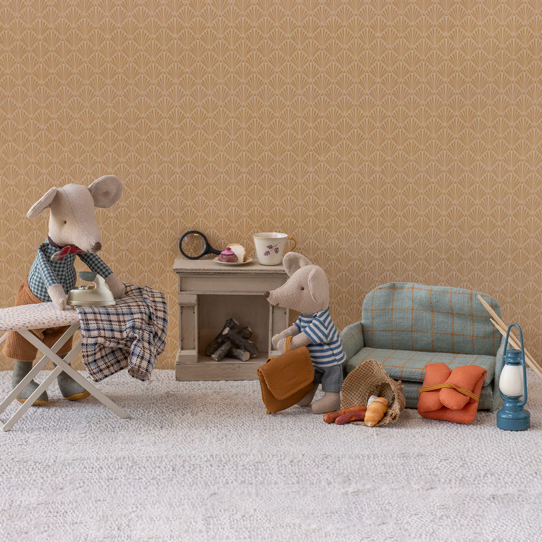 Miniature diorama with toy mice and furniture against a beige wall.