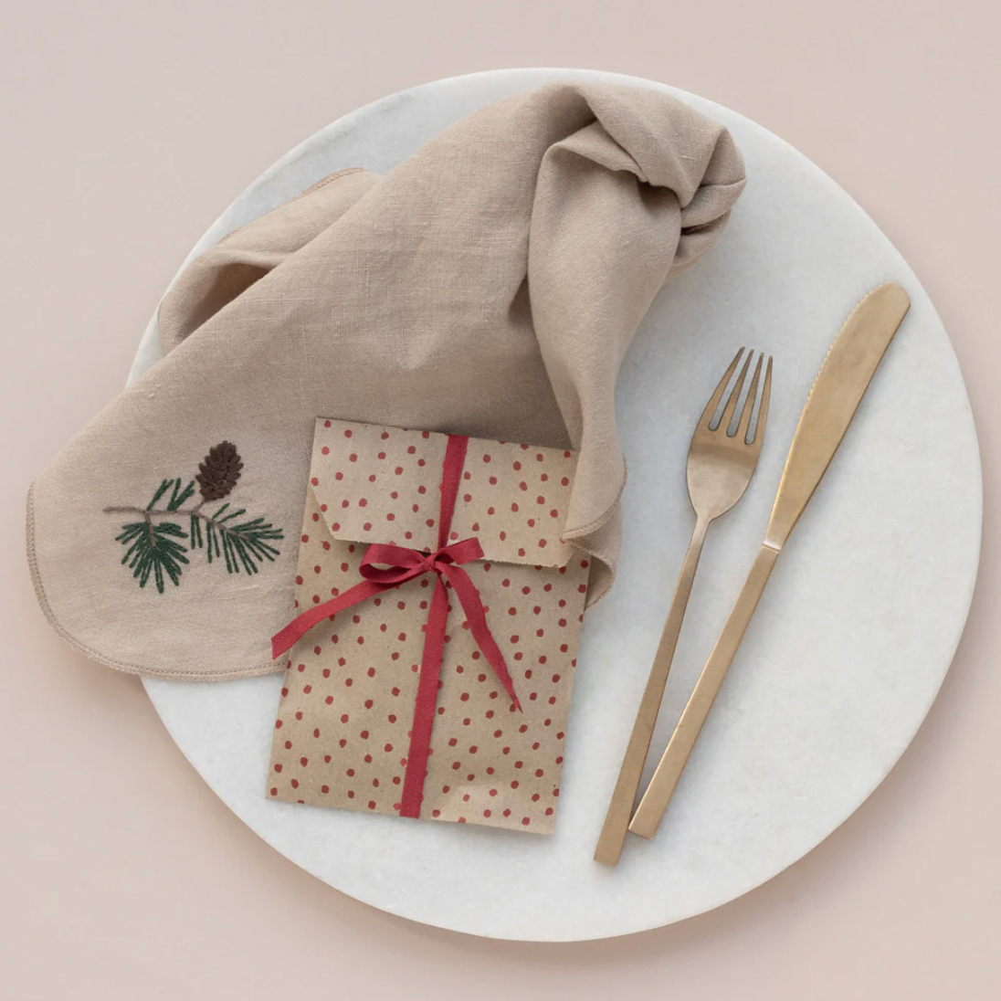 Plated setting with folded napkin, wrapped gift, fork, and knife on a beige background