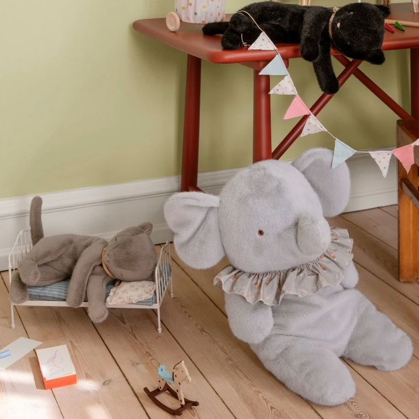Gray plush elephant toy on a wooden floor with a child's play area in the background