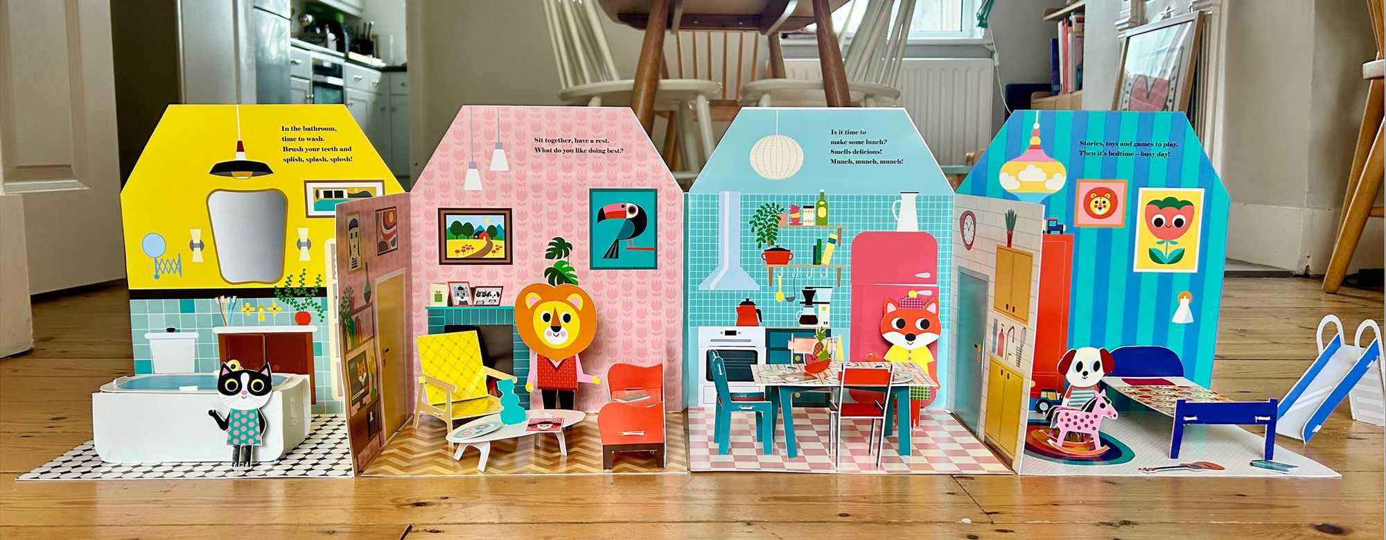 Colorful toy houses with furniture and decorations on a wooden floor.