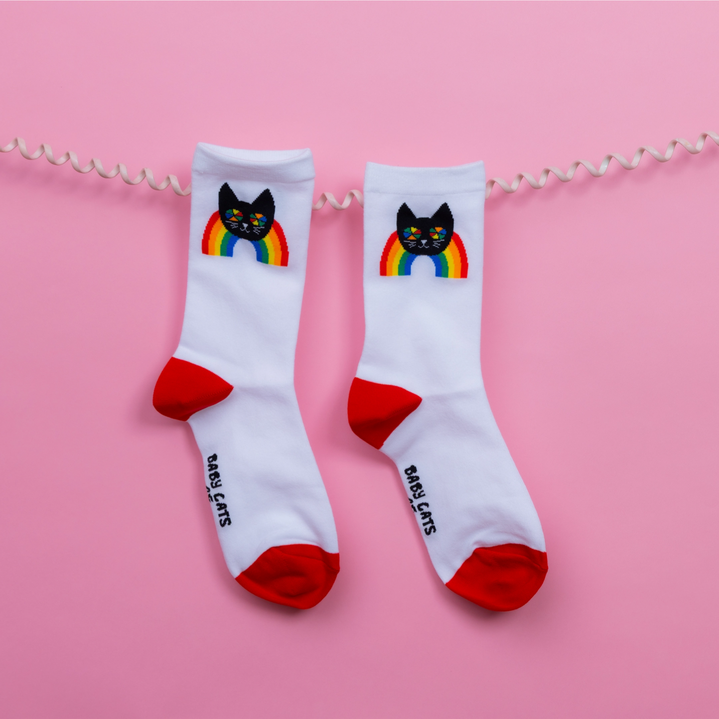 White socks with black cat and rainbow design on red toes against a pink background