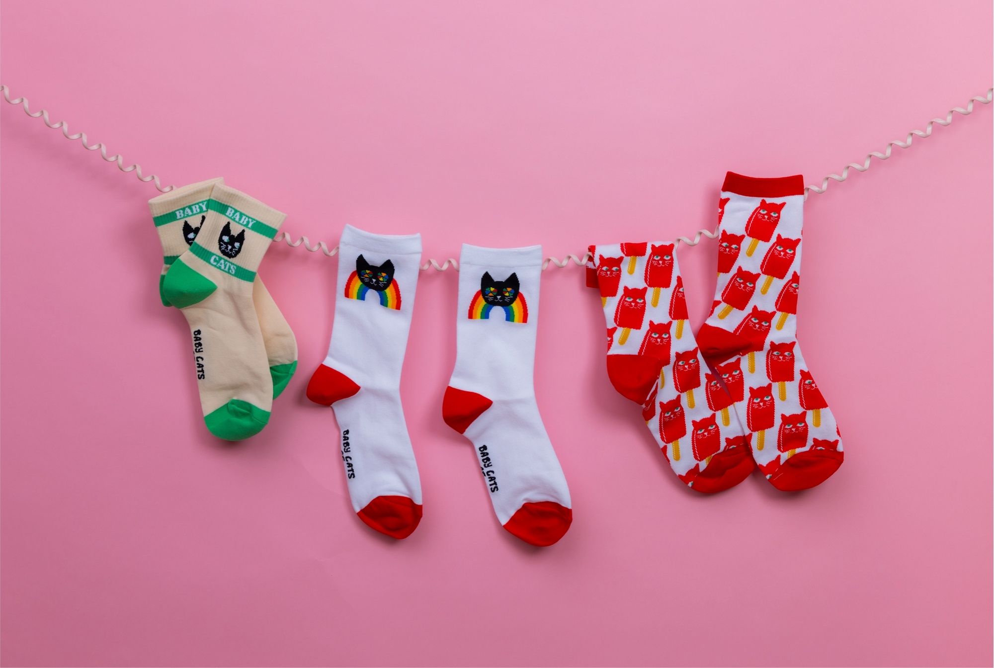 Four pairs of socks with cat designs on a pink background
