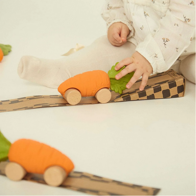 Child playing with orange toy cars on a cardboard track