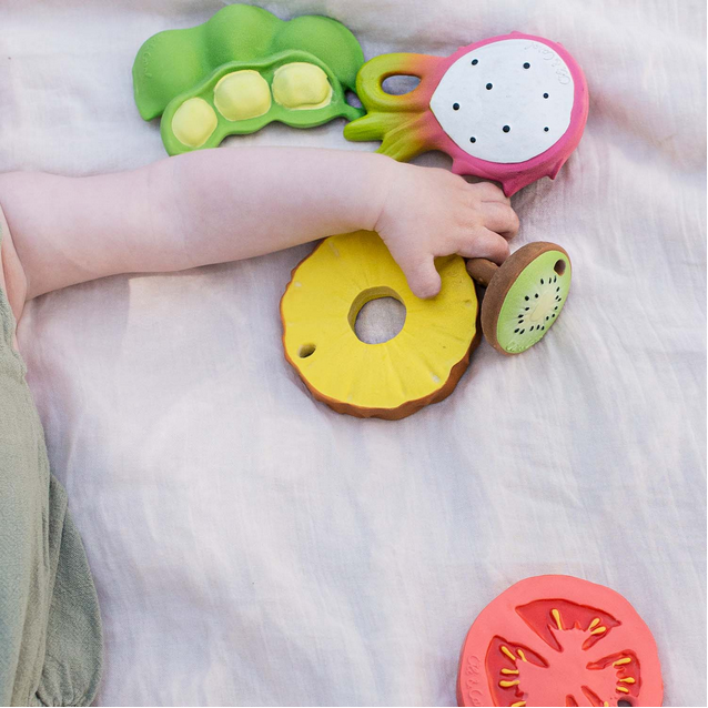 Colorful fruit-shaped baby teething toys on a soft surface with a child's hand reaching out.
