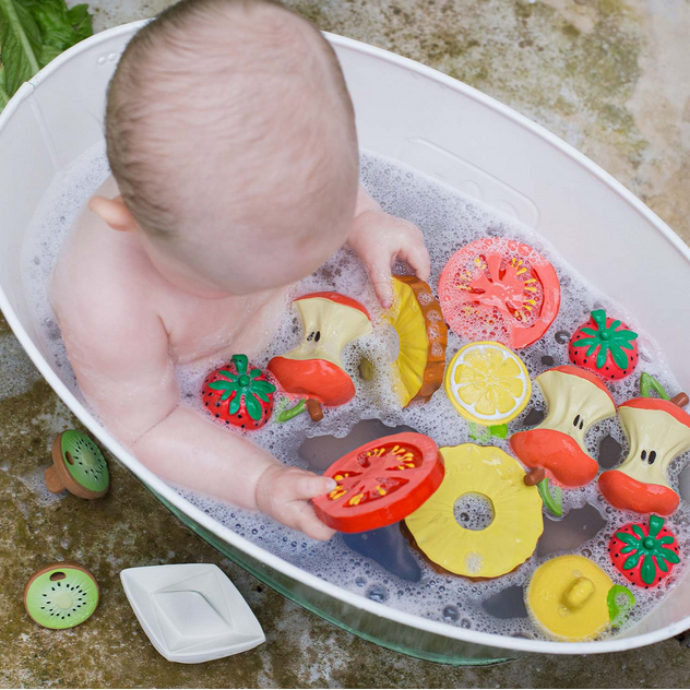 Baby playing with colorful vegetable-shaped bath toys in a bathtub.
