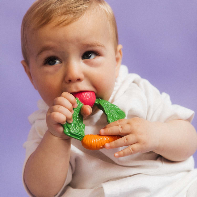 Baby holding and chewing on a colorful toy against a purple background