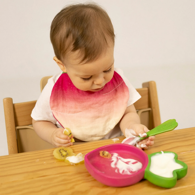 Child in a high chair with a colorful bib, eating at a table.
