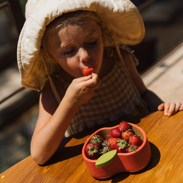 Child eating strawberries from a heart-shaped container on a wooden table