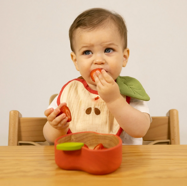 Baby eating a strawberry at a wooden table with a plain background