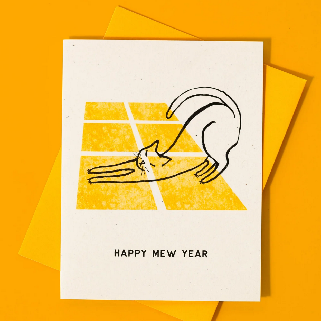Greeting card with a stylized cat on a yellow background and 'Happy New Year' text, placed on an orange surface.