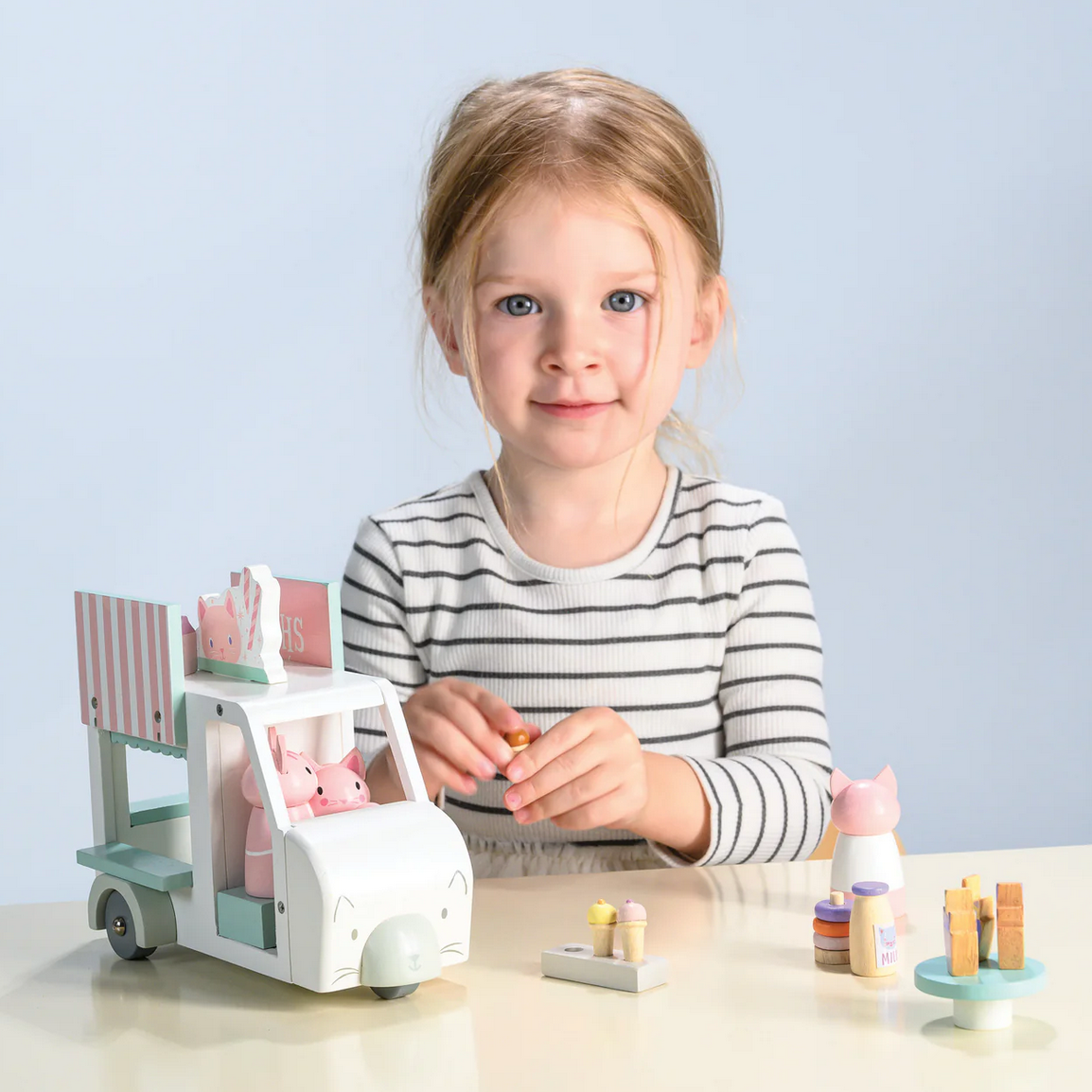 Child playing with a toy ice cream truck and figurines on a light blue background