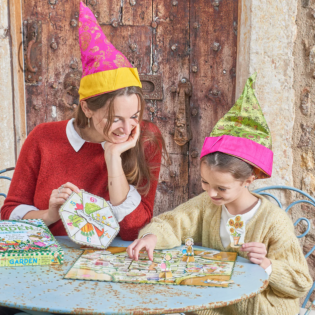Two people wearing colorful party hats playing a board game outdoors.