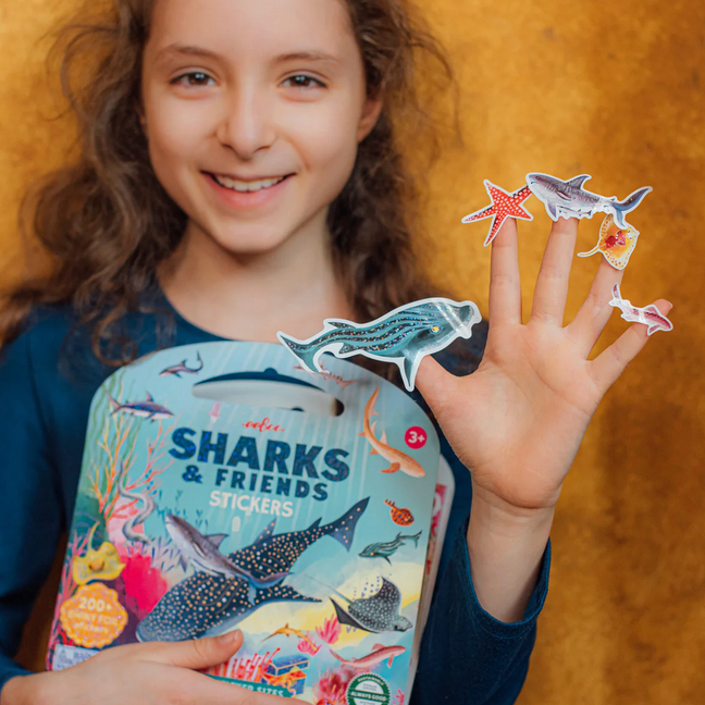 Child holding a pack of 'Sharks & Friends' stickers with a few on their finger.