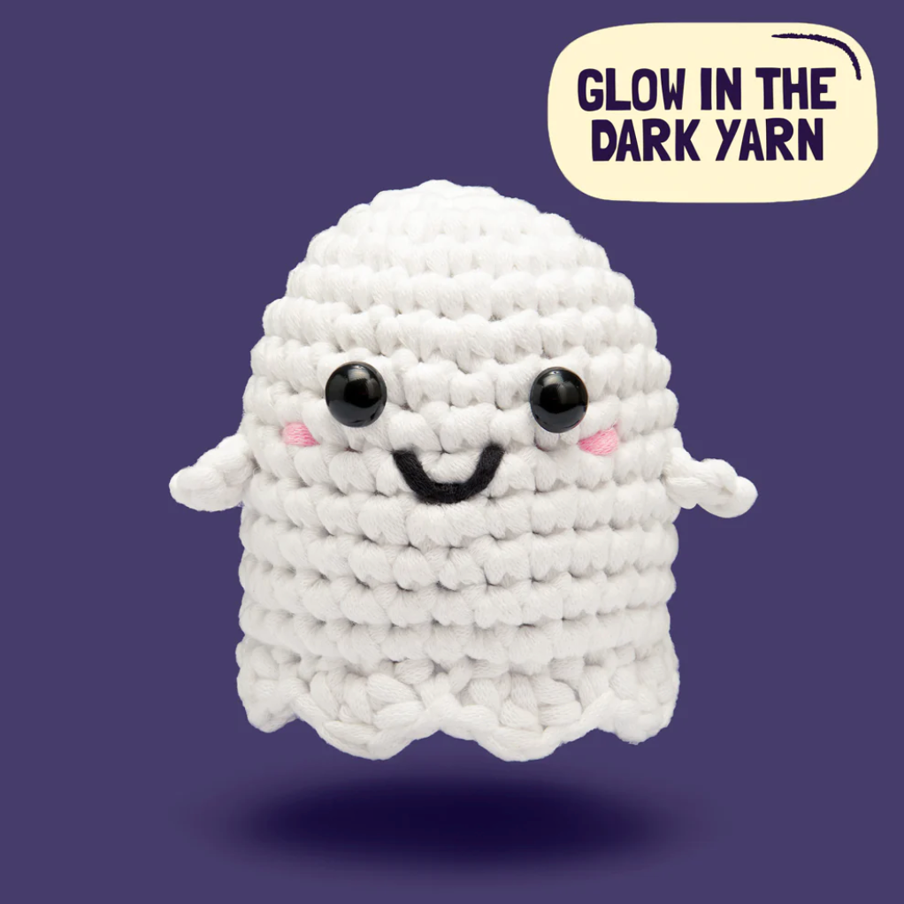 White crochet ghost with black eyes and a smile on a dark blue background, labeled 'Glow in the Dark Yarn'.