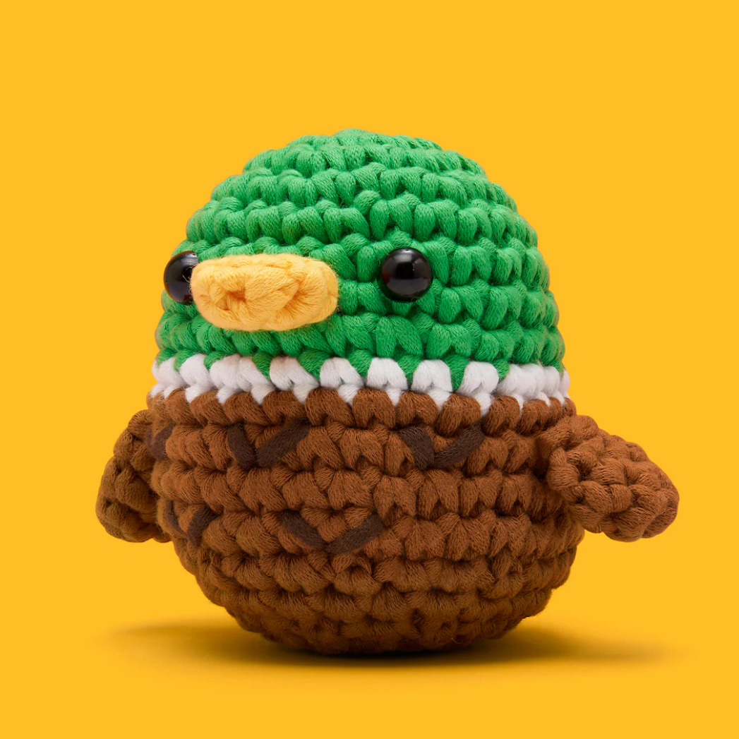Crocheted toy resembling a bird with green head and brown body on a yellow background