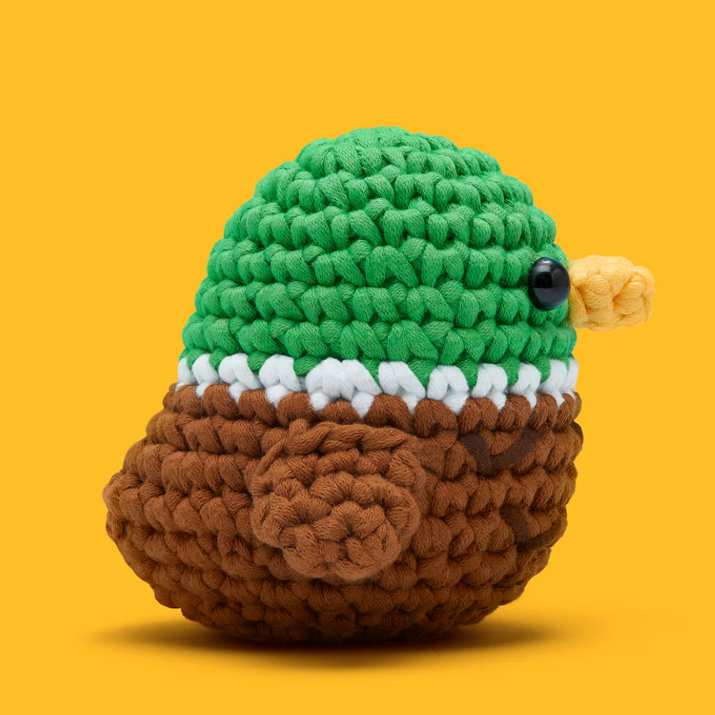 Crocheted turtle toy with green shell, brown body, and black eye on a yellow background
