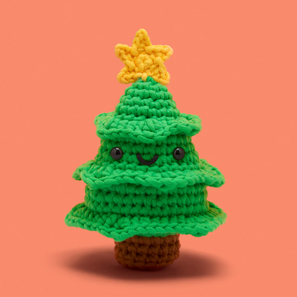Crocheted Christmas tree toy with a yellow star on a peach background