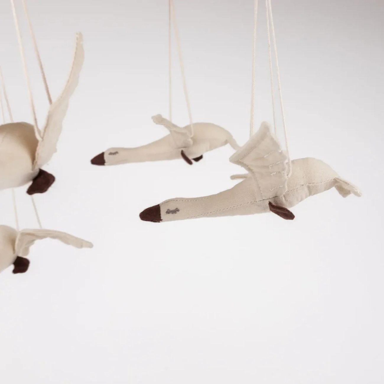 Plush toy swans hanging from strings against a white background