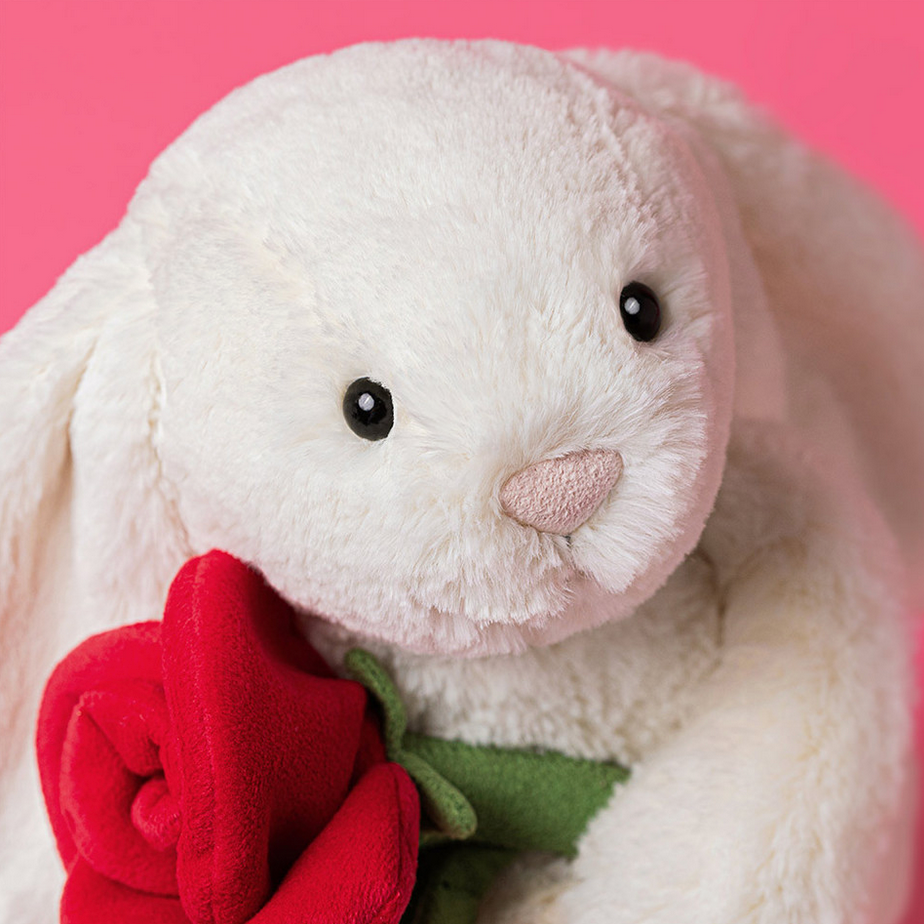 Plush bunny toy with a red rose on a pink background