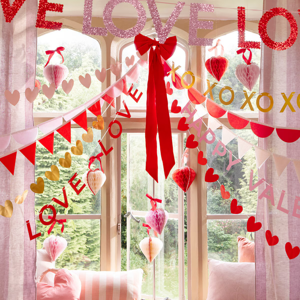 Decorative window with 'LOVE' and heart shapes for Valentine's Day, with a red bow and pink striped cushions.