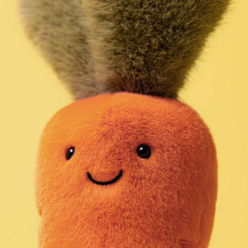 Plush carrot toy with a smiling face on a yellow background