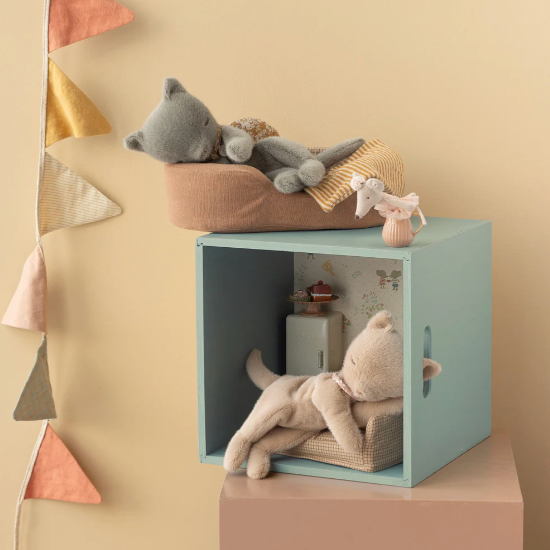 Children's room with a light blue cube shelf, plush toys, and decorative pillows on a beige wall.