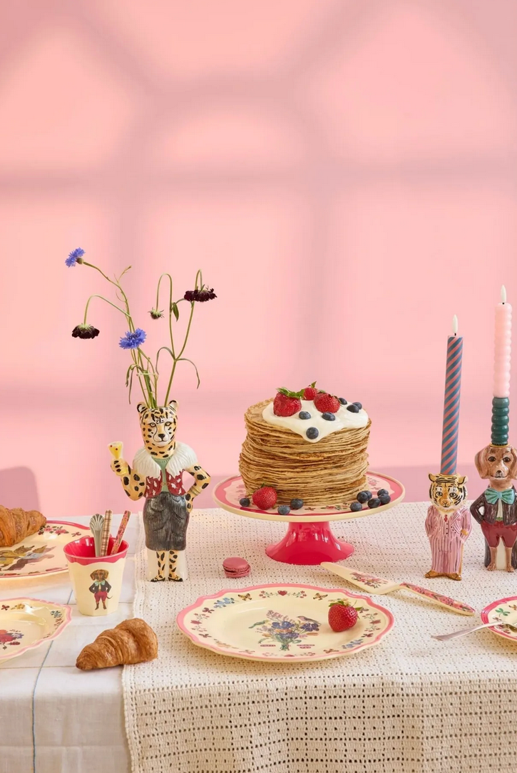 Table setting with a cake, croissants, and decorative items against a pink wall.