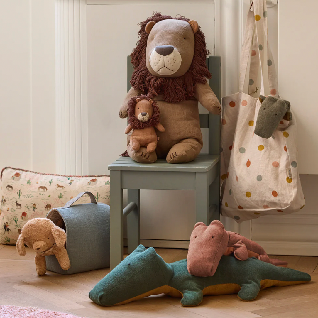 Children's toys including a lion, teddy bear, and dinosaur on a wooden floor with a neutral-colored wall in the background.