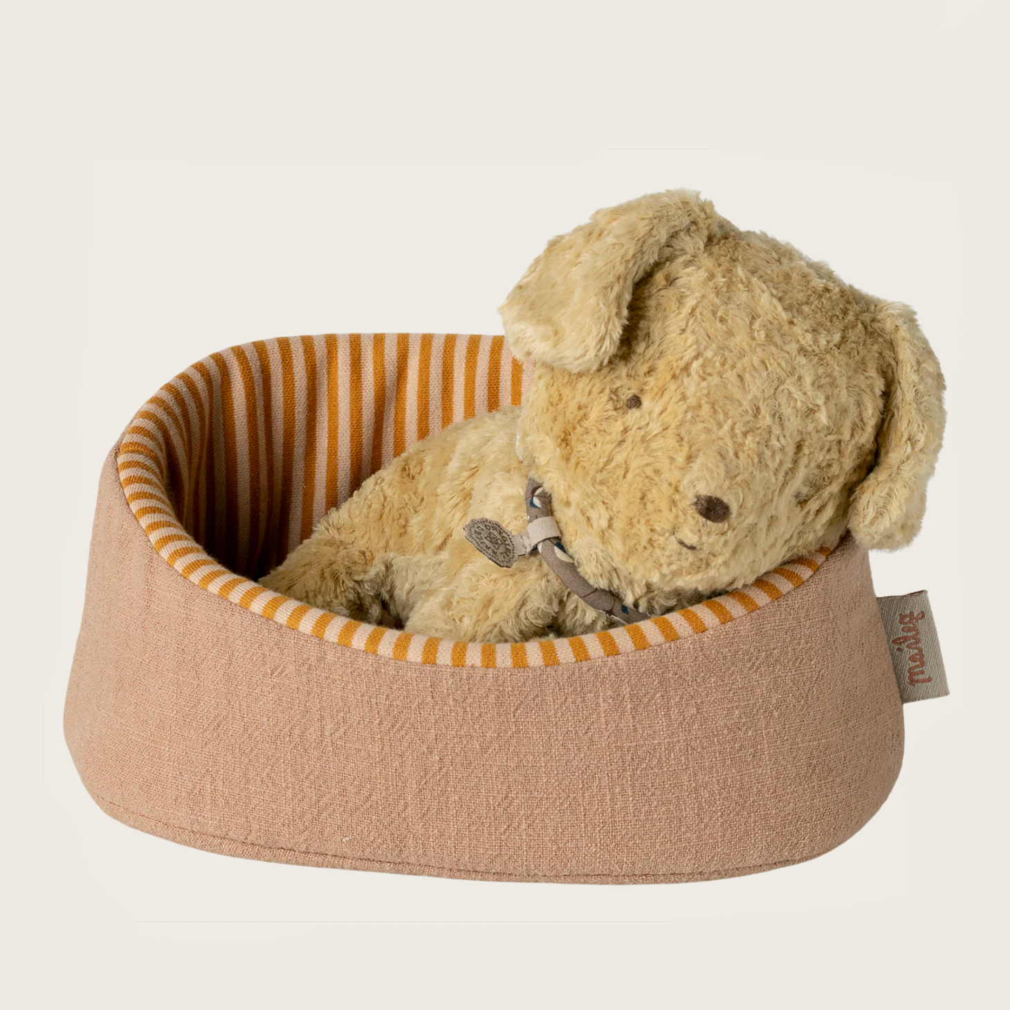 Plush puppy in a brown pet bed with orange striped lining on a beige background