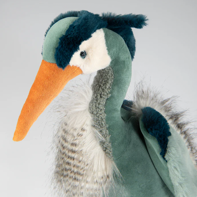 Stuffed toy heron with a green body, orange beak, and black head on a light gray background
