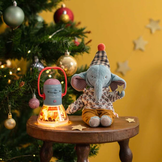 Plush elephant toy with a lantern next to a Christmas tree