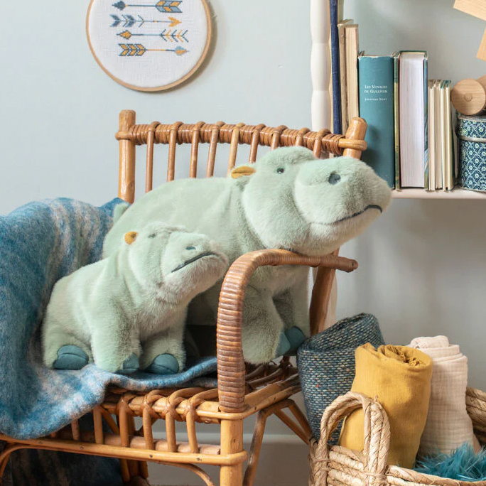 Two green plush dinosaurs on a wicker chair with a cozy room setting.