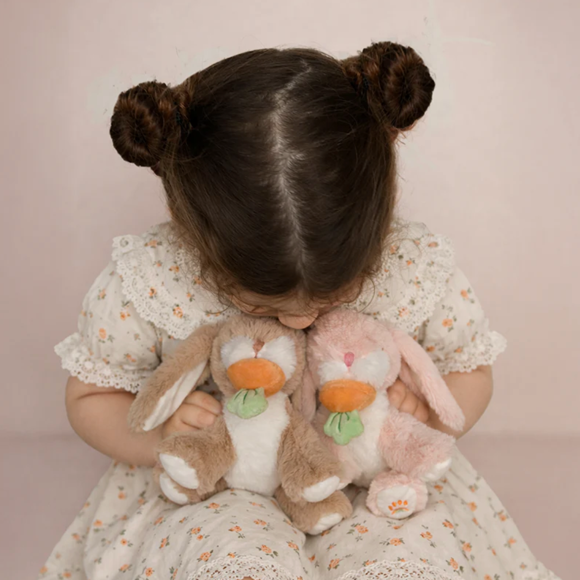 Child holding three plush bunnies against a plain background