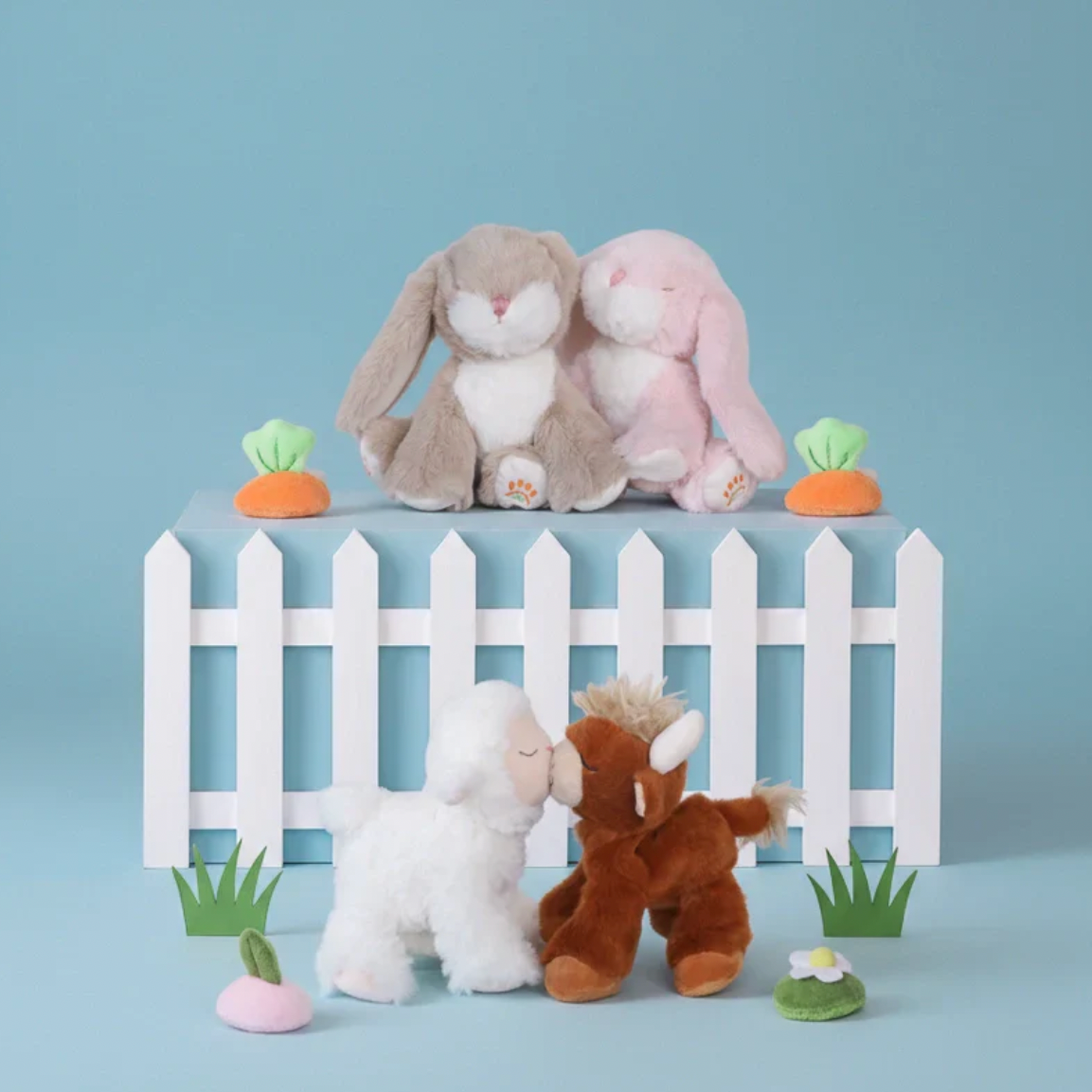 Plush toys including a rabbit, sheep, and goat in front of a white picket fence on a blue background.