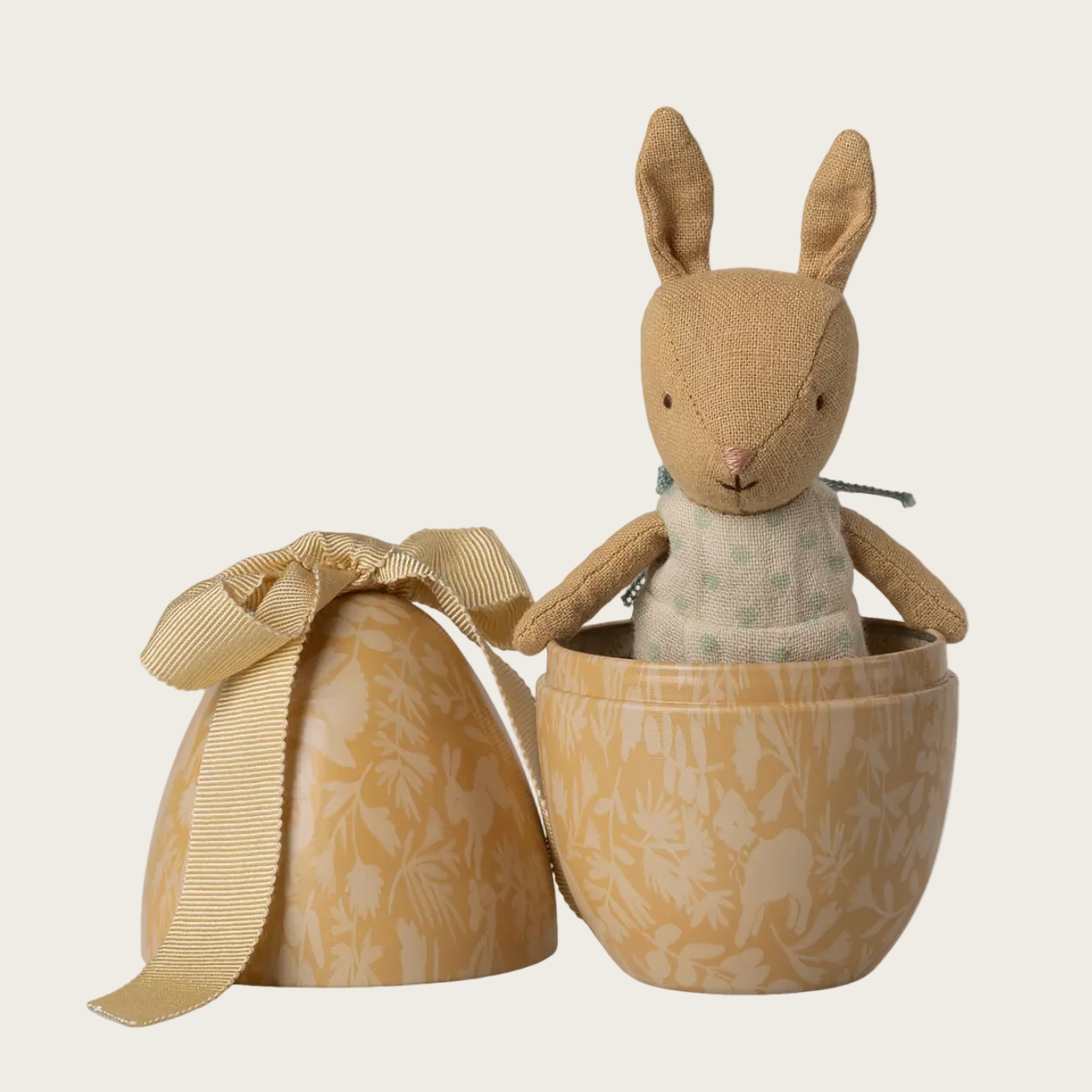 Stuffed rabbit toy in an open metal egg on a white background