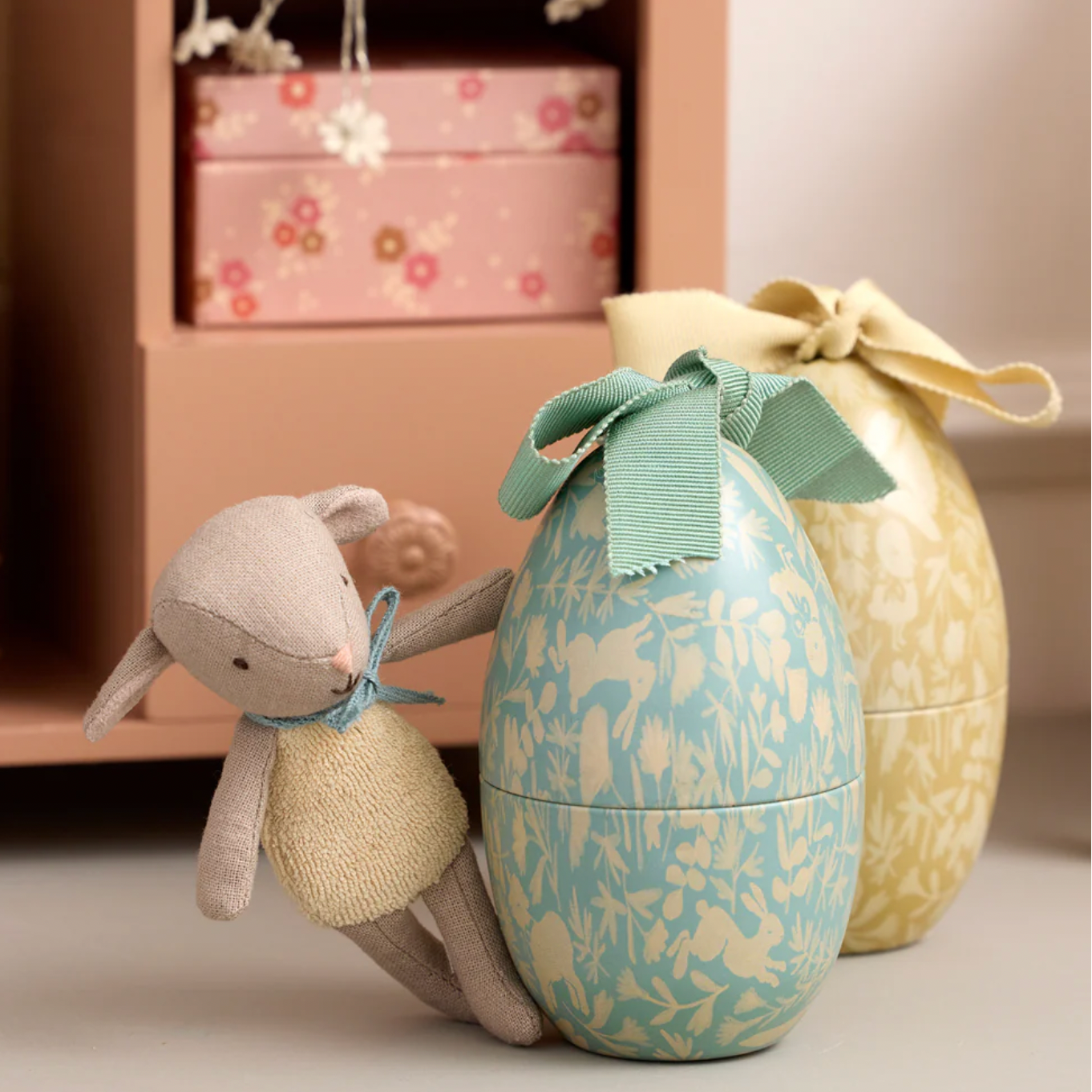 Decorative egg with floral pattern and bow next to a plush toy on a surface.
