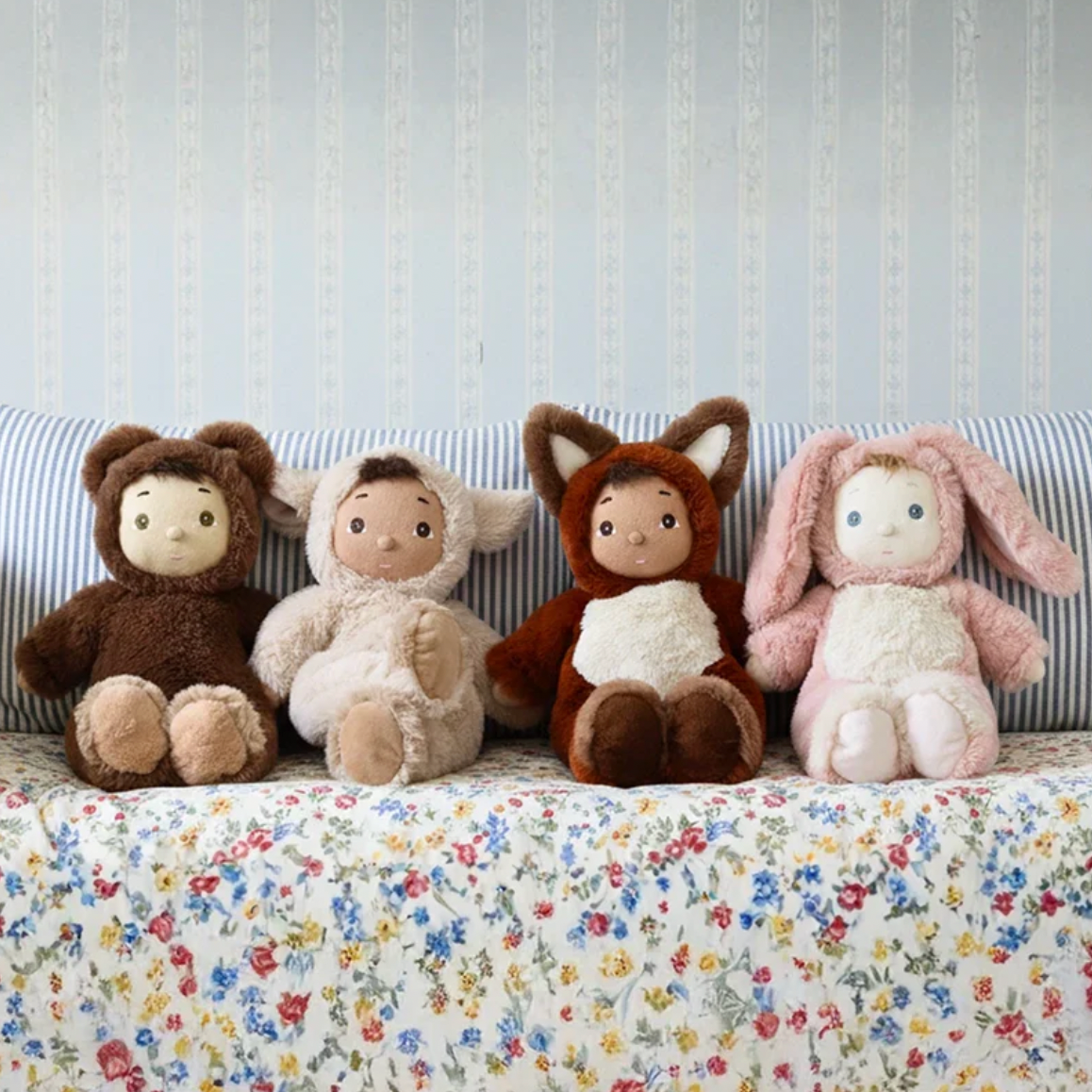 Four plush toys on a bed with a floral blanket and striped headboard