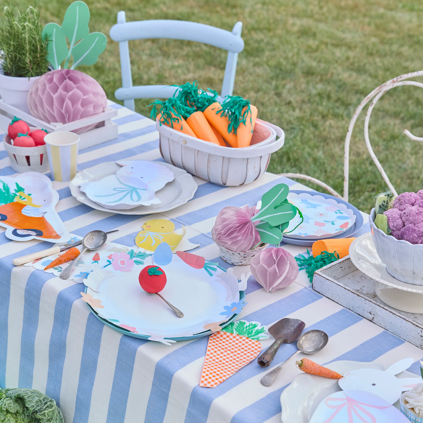 Children's table setting with garden-themed decorations on a striped tablecloth outdoors.