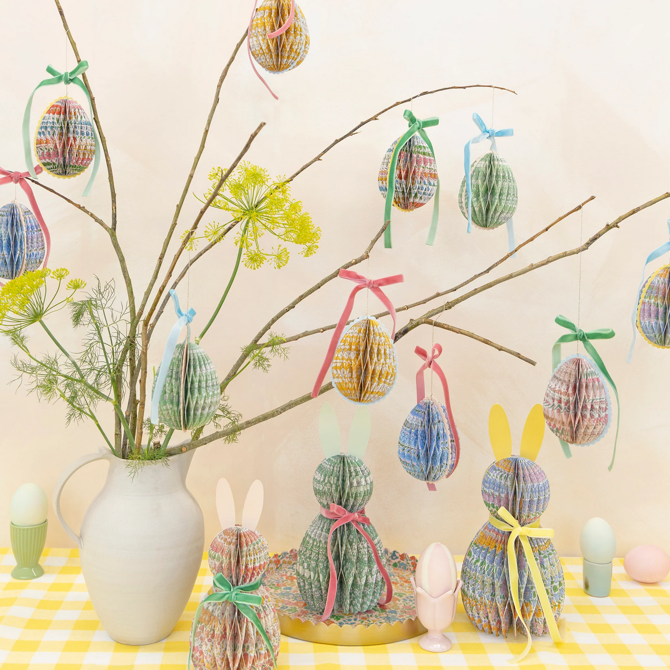 Decorative Easter scene with paper eggs, bunny figures, and a vase on a checkered tablecloth.