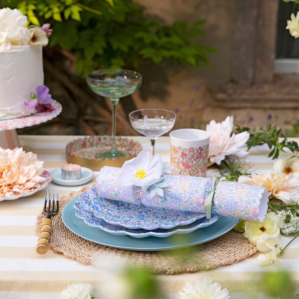 Elegant table setting with floral plates, napkins, and glasses on a striped tablecloth.