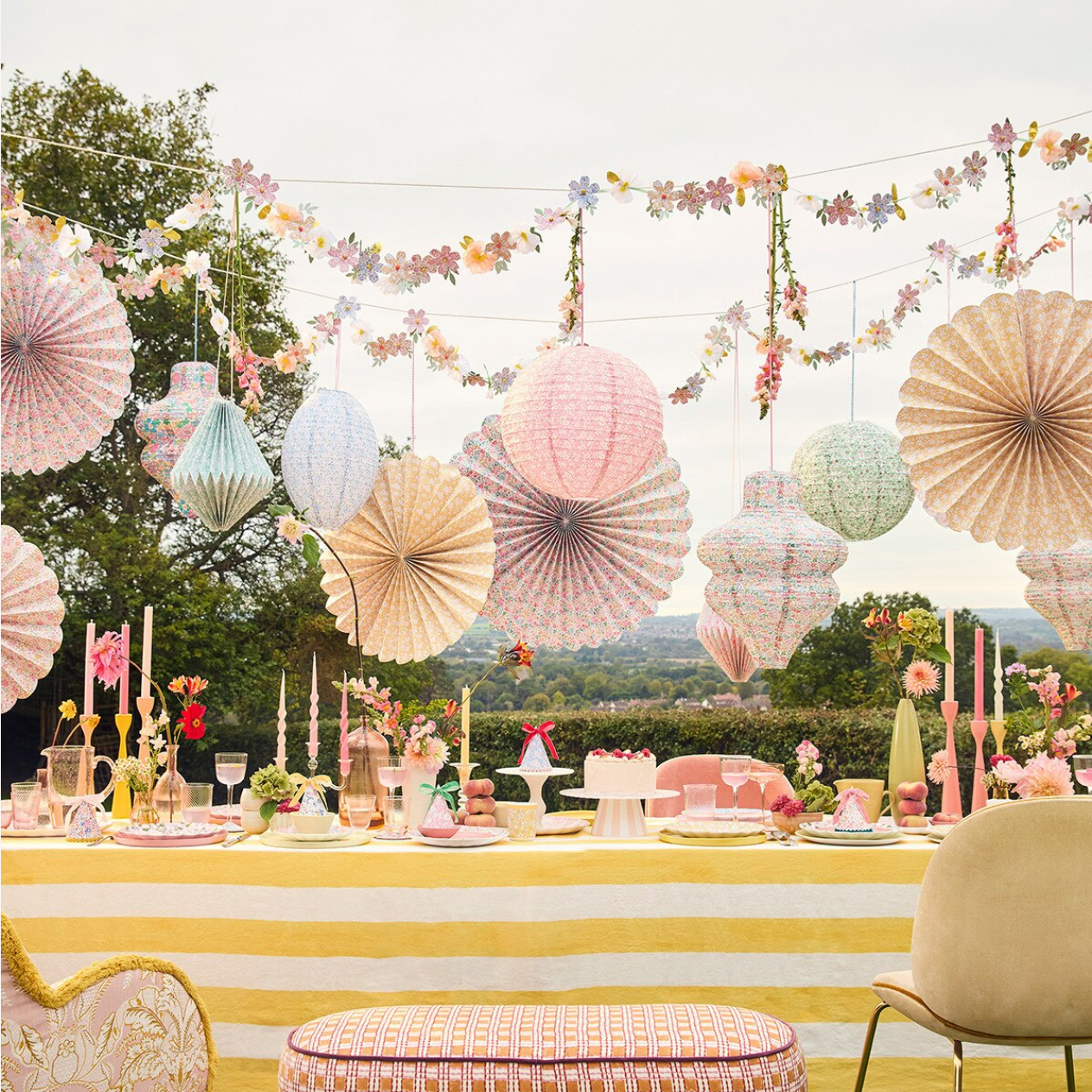 Decorative outdoor setting with hanging paper fans and floral garlands.