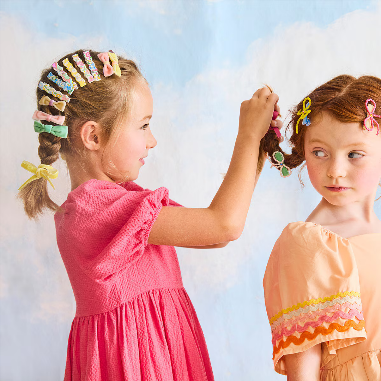 Two young girls with colorful hair clips against a light blue sky.