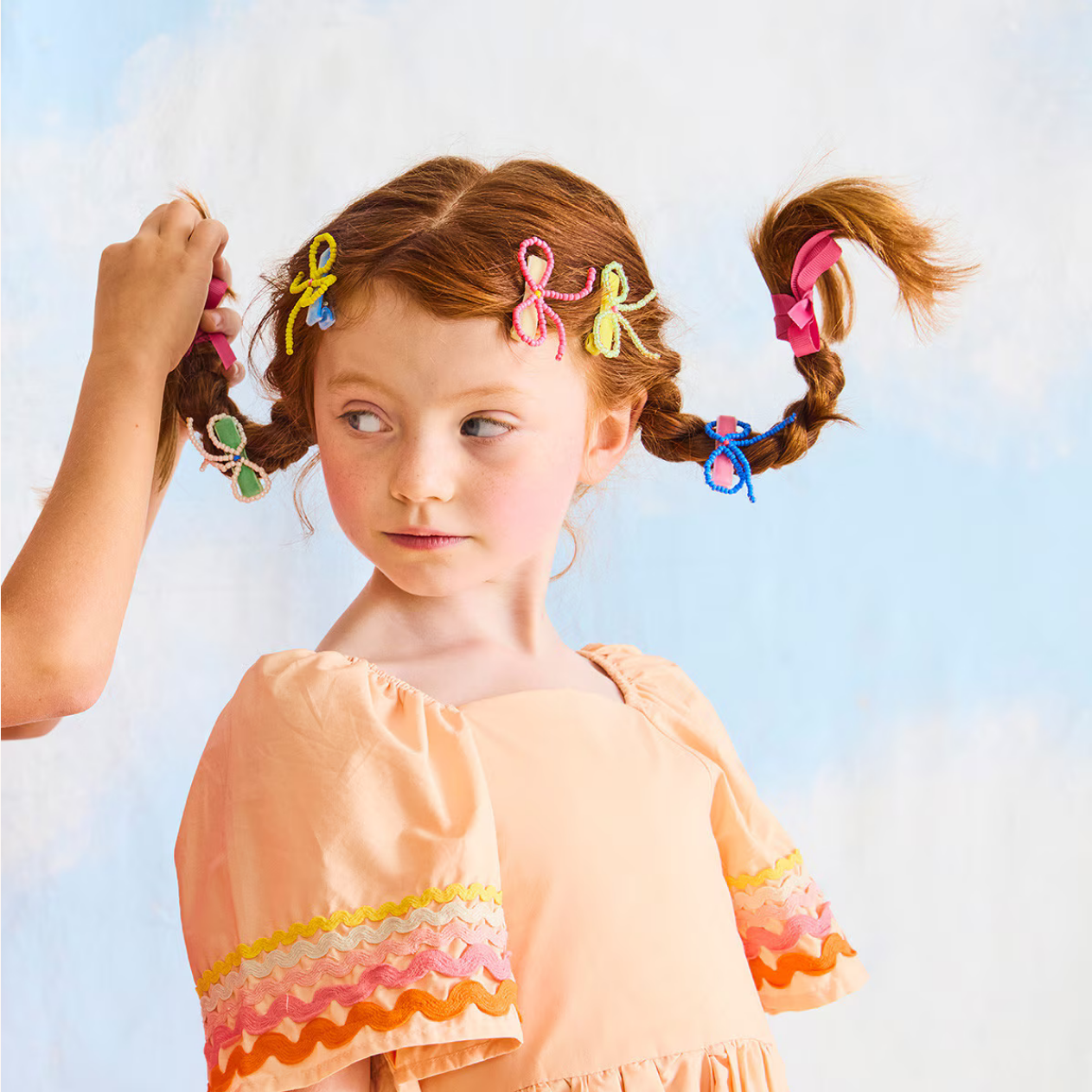 Young girl with colorful hair clips in her pigtails against a light blue sky.