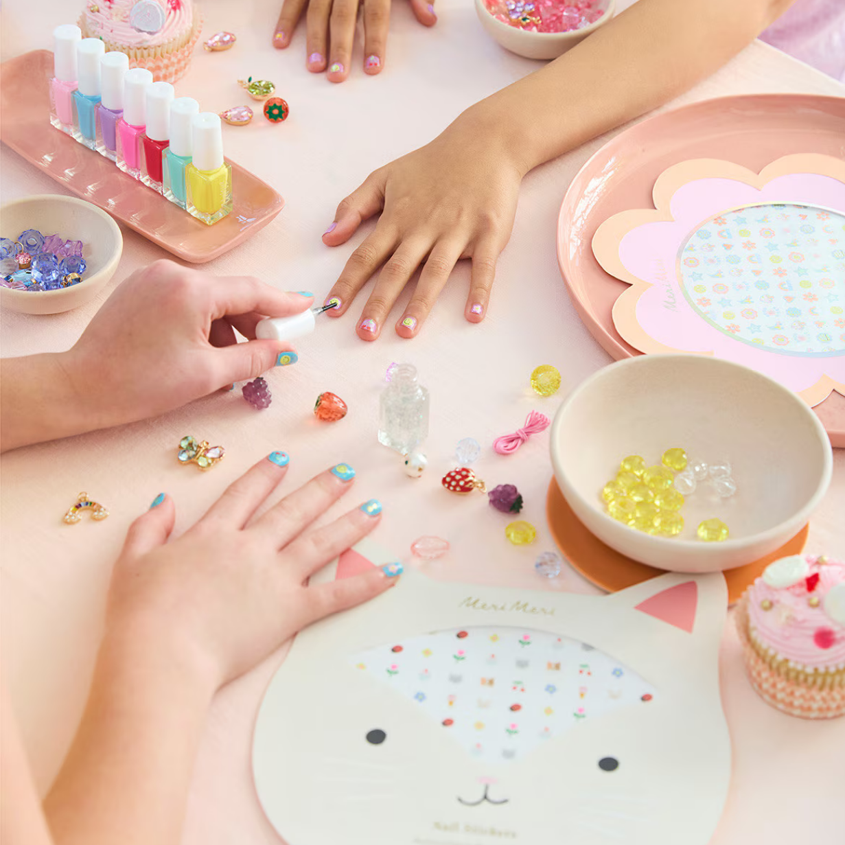 Children's hands with colorful nail polish and decorative items on a table.