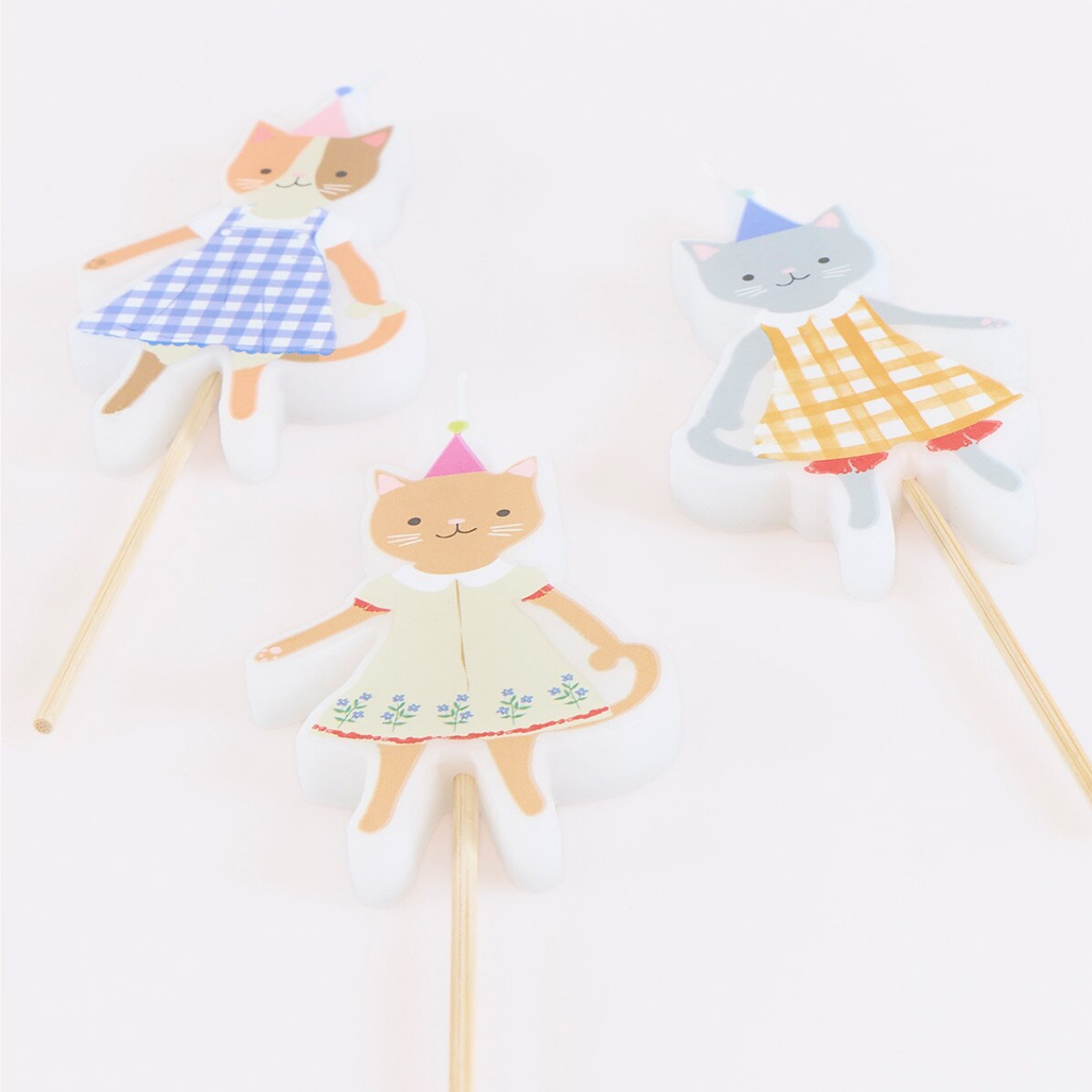 Three paper dolls on sticks with colorful dresses on a white background