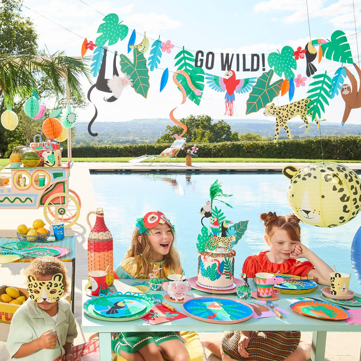 Children at a pool party with jungle-themed decorations and 'GO WILD!' banner.
