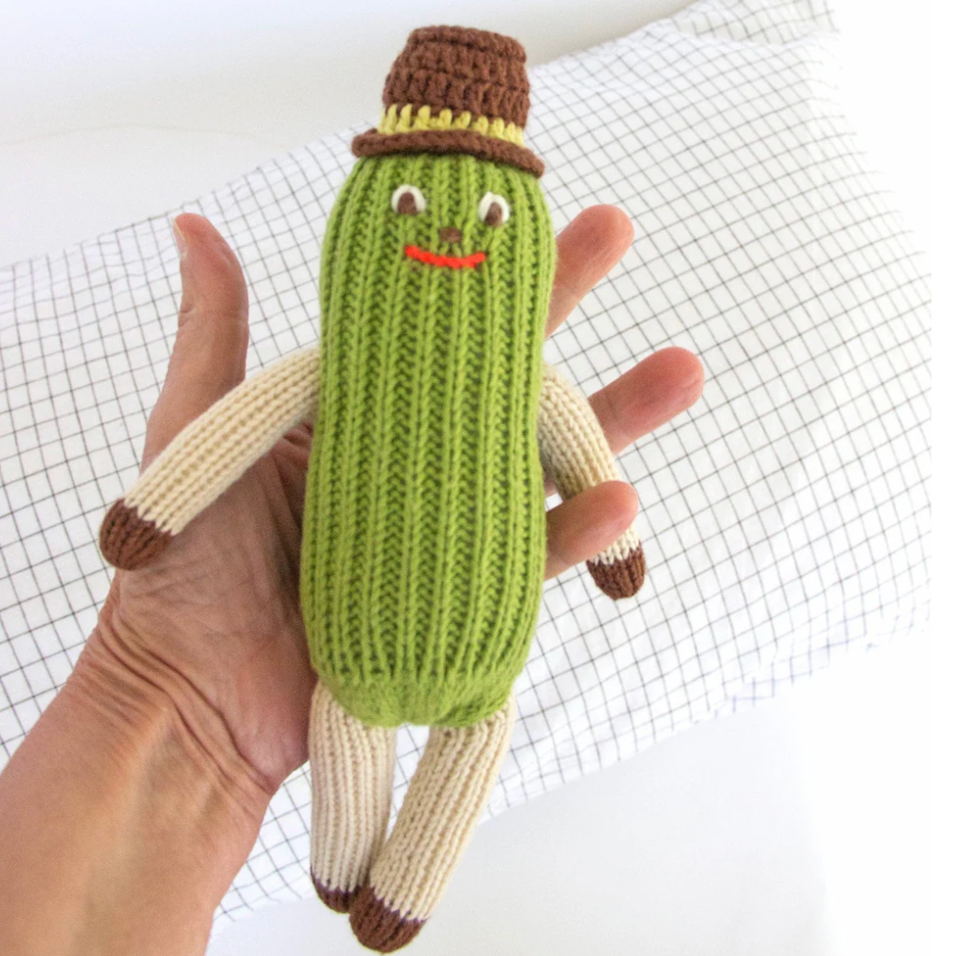 Hand holding a knitted pickle toy with a brown hat on a white background