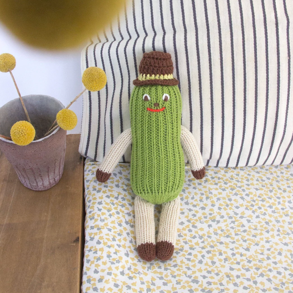 Knitted pickle toy with a hat on a patterned surface