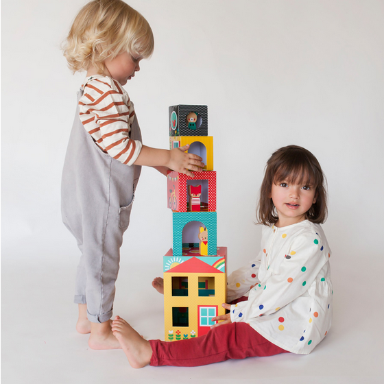 Two children playing with a colorful tower of blocks against a white background